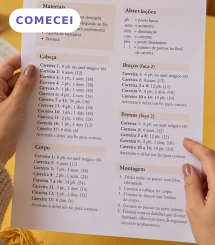 Mãos segurando uma receita de amigurumi impressa, com o rótulo COMECEI